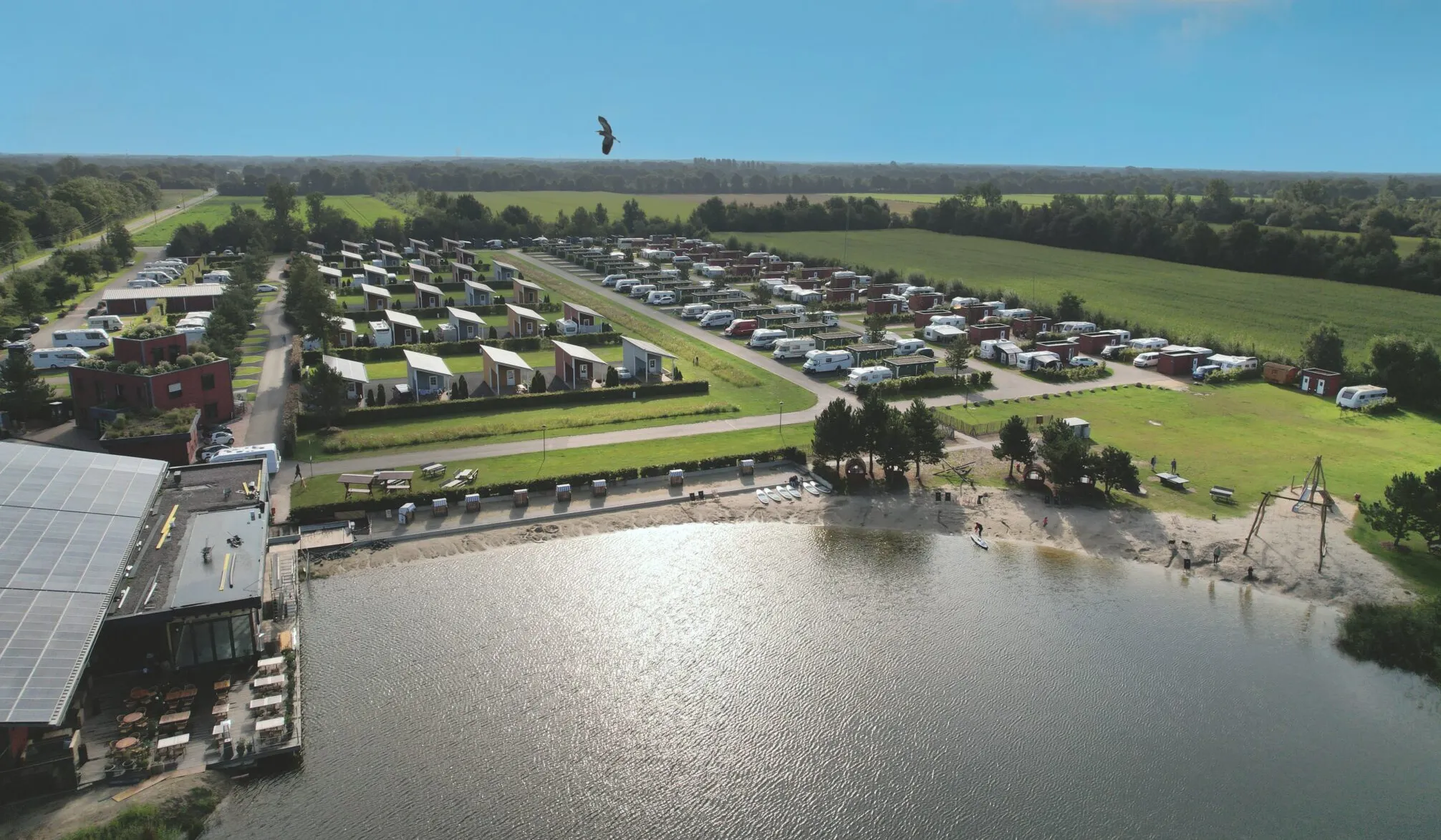 Aerial view of Emsland camping site with caravans and pitches beside a lake.