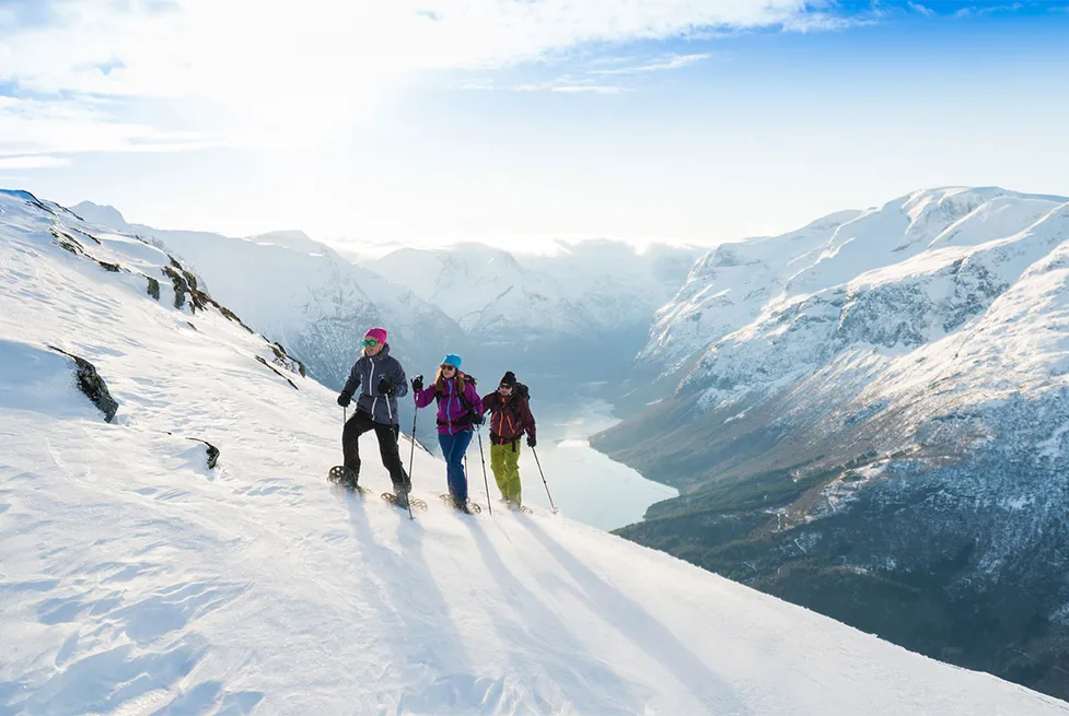 Three snowshoe hikers traverse a snow-covered mountainside above a fjord near Stryn, Norway.