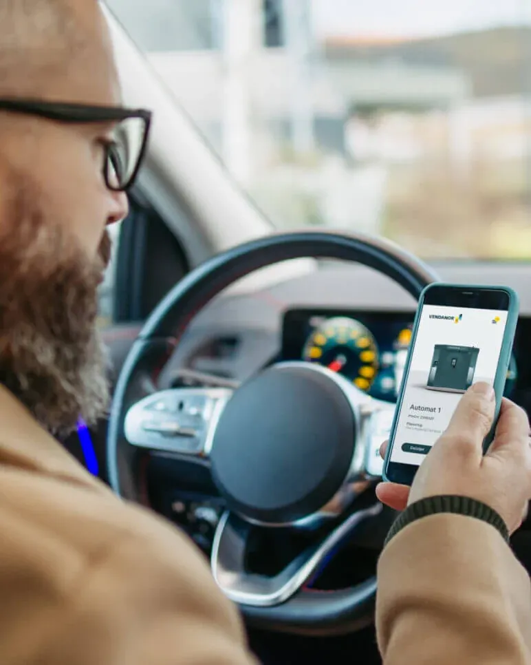 Driver in a car viewing a Propane Vending Machine in the Vendanor Connect app on a smartphone.