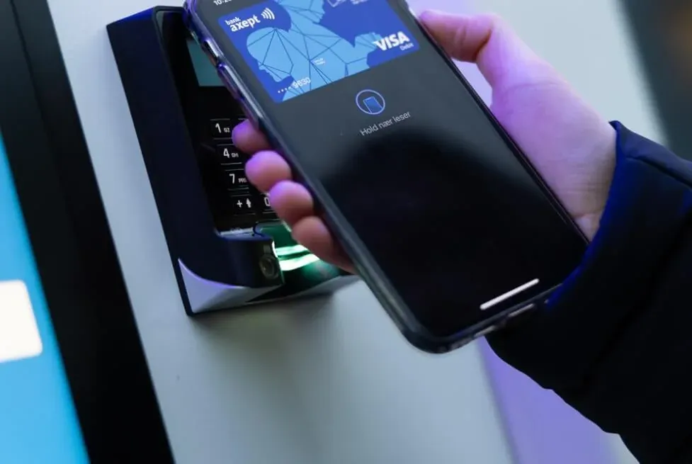 Customer paying at a Vendanor machine payment terminal by holding a smartphone with Visa contactless card to the reader.
