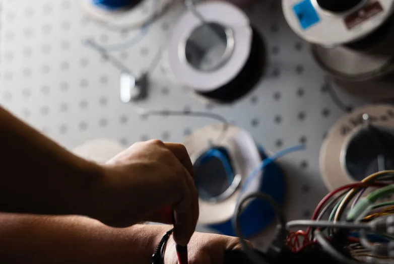 Close-up of hands assembling wiring next to colored cable spools during Vendanor electronics production.