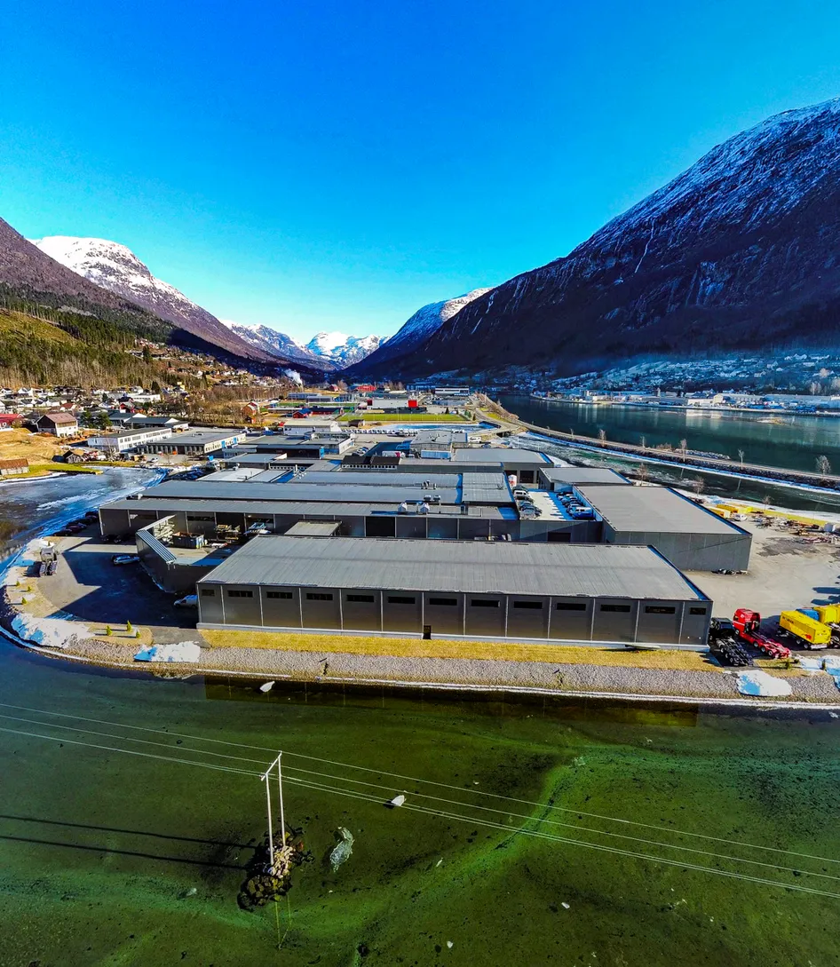 Aerial view of the Vendanor factory on a fjord shore surrounded by snow-capped mountains.