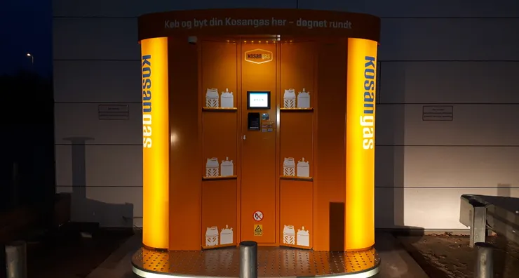 An illuminated orange Kosangas-branded Vendanor Propane Vending Machine glows at night outside a building.