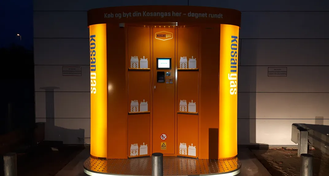 An illuminated orange Kosangas-branded Vendanor Propane Vending Machine glows at night outside a building.
