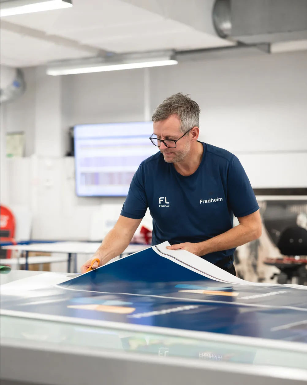 Production worker handling a printed panel at a workbench in a Vendanor production facility.