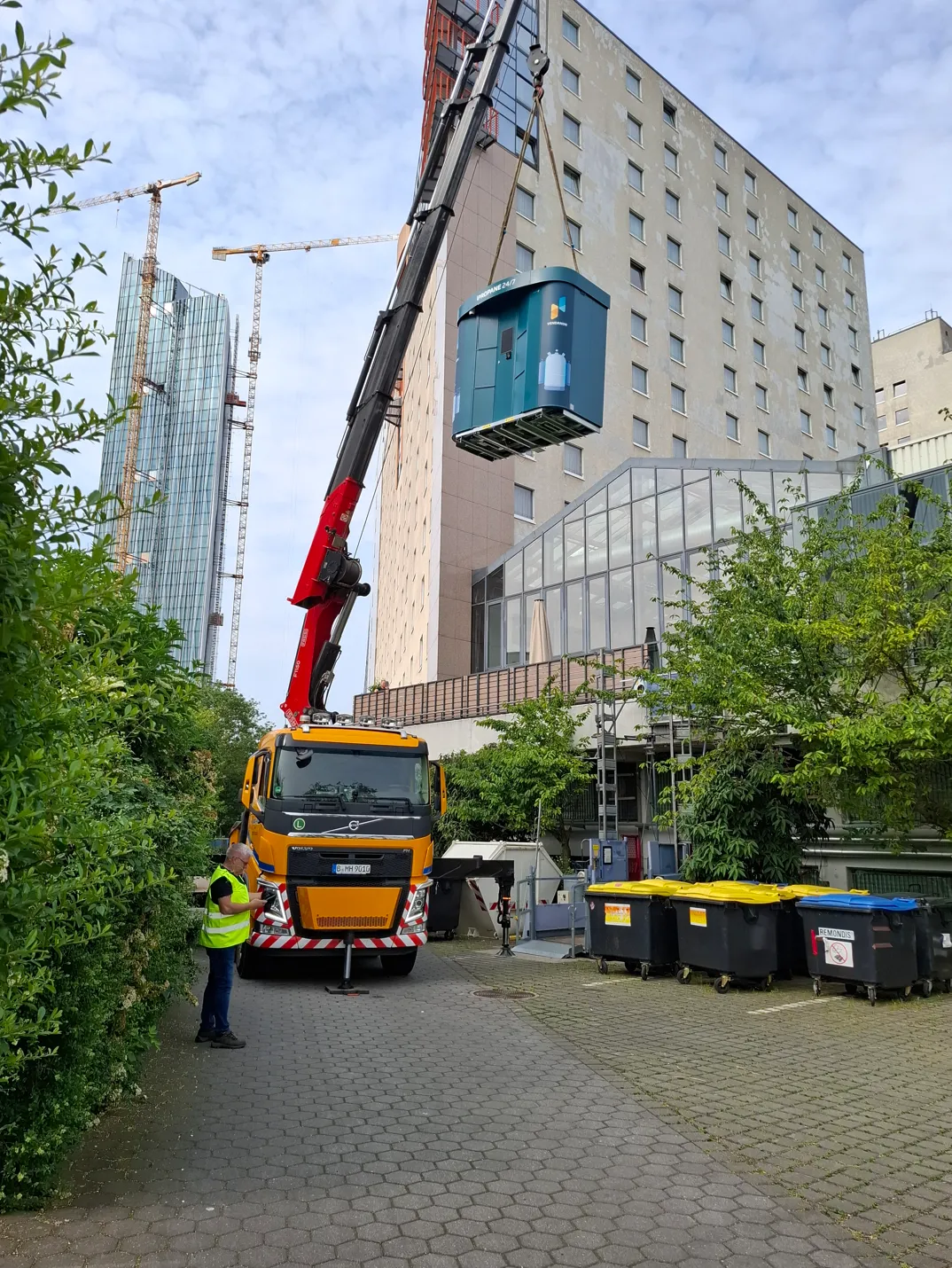 Crane lifting a Vendanor Propane Vending Machine into place next to a tall building.