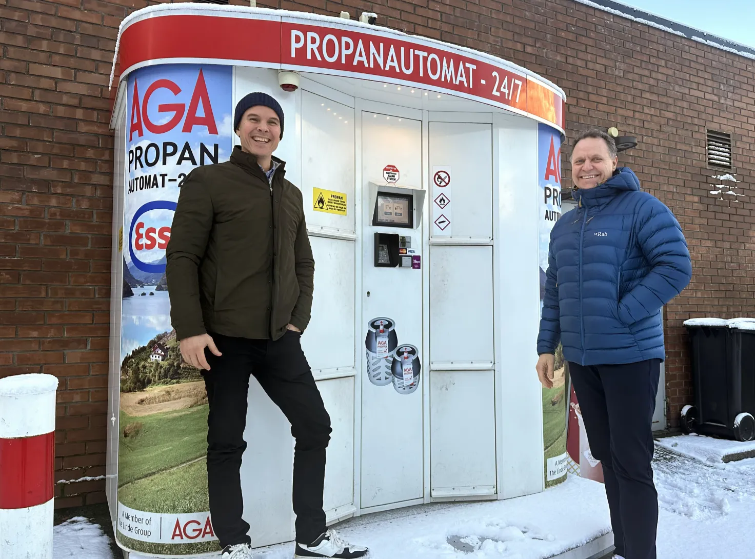 Two men standing beside an AGA-branded Vendanor Propane Vending Machine at an Esso station in Stryn in winter.