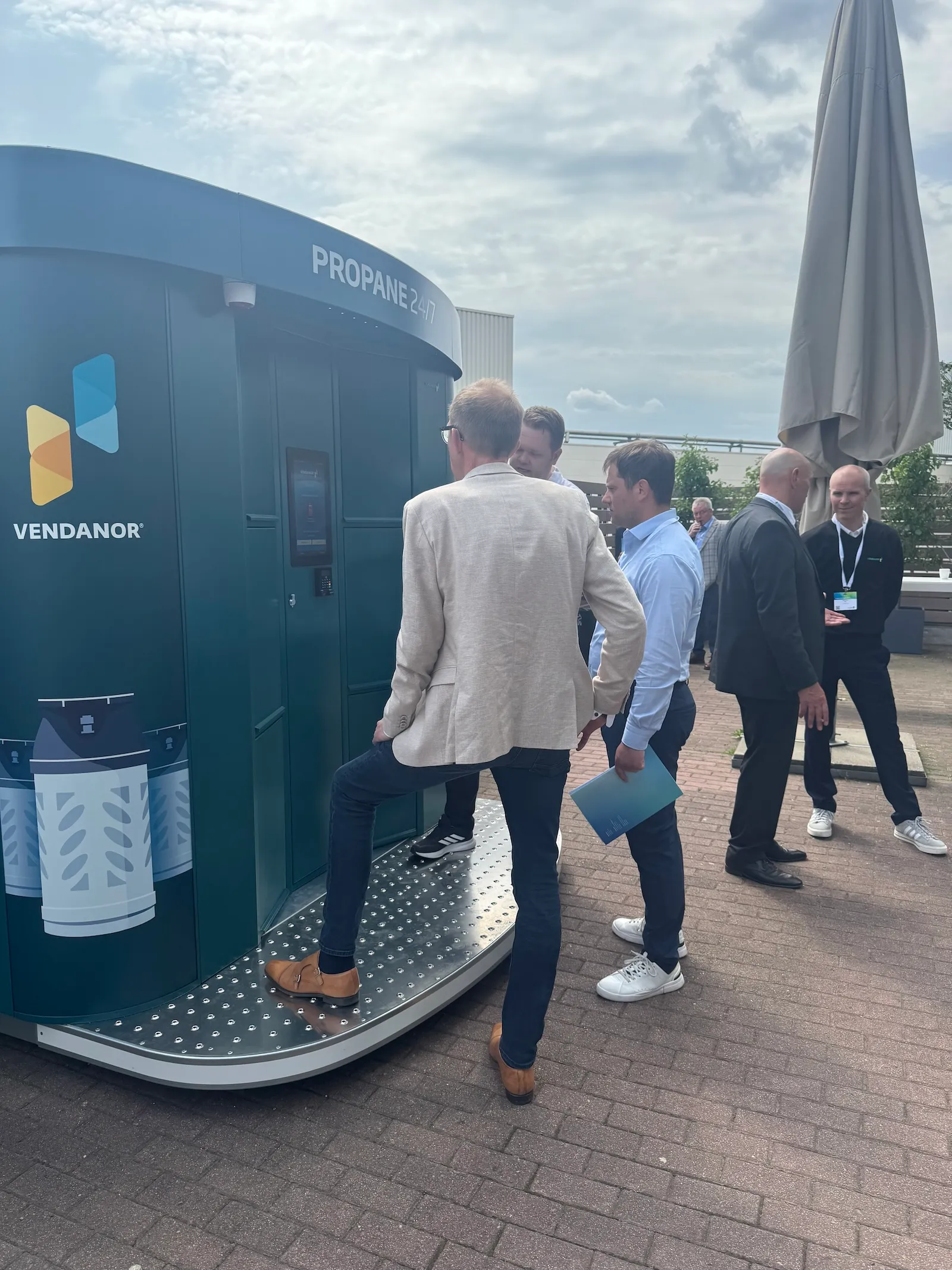 A man stepping onto the platform of a Vendanor Propane Vending Machine during an outdoor trade fair demonstration.