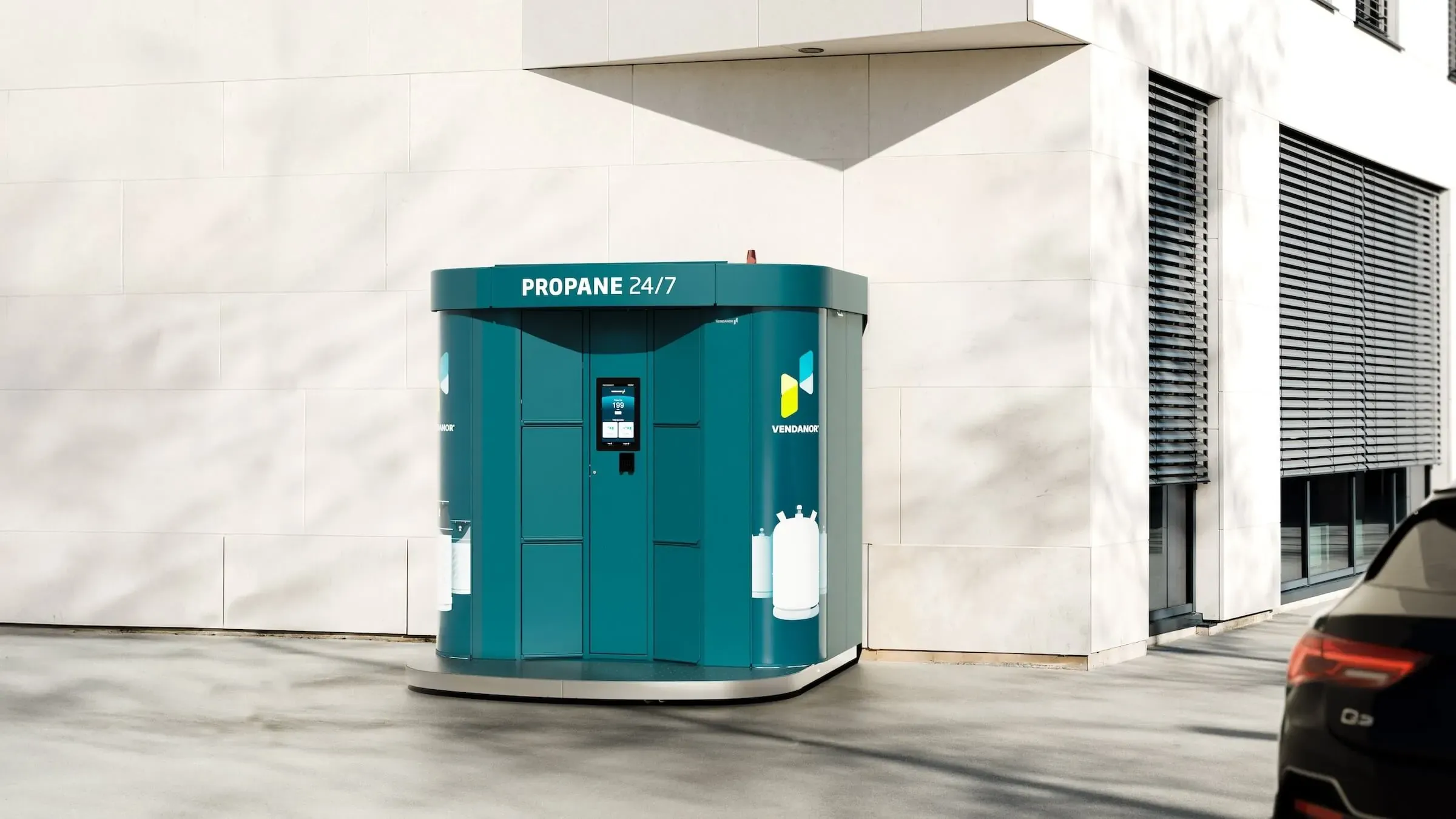 A teal Vendanor Propane Vending Machine labelled Propane 24/7 stands outside a modern building next to a parked car.