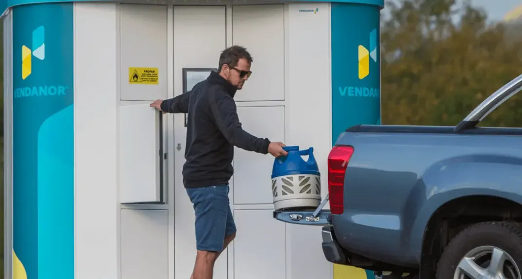 A man taking a propane cylinder from a Vendanor Propane Vending Machine to load into a pickup truck.