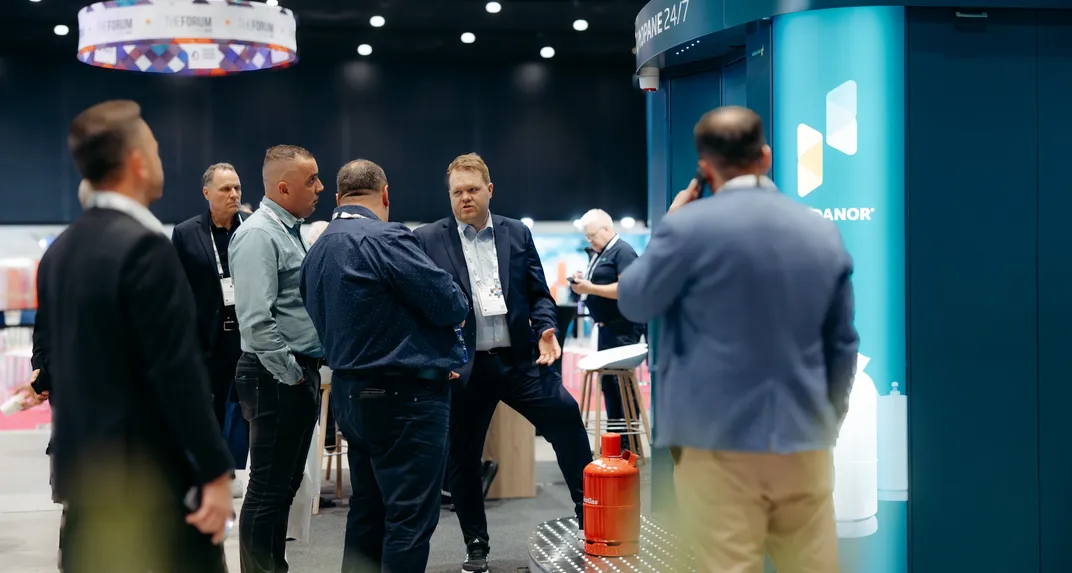 Visitors talking beside a Vendanor Propane Vending Machine with a propane cylinder at a trade fair stand.