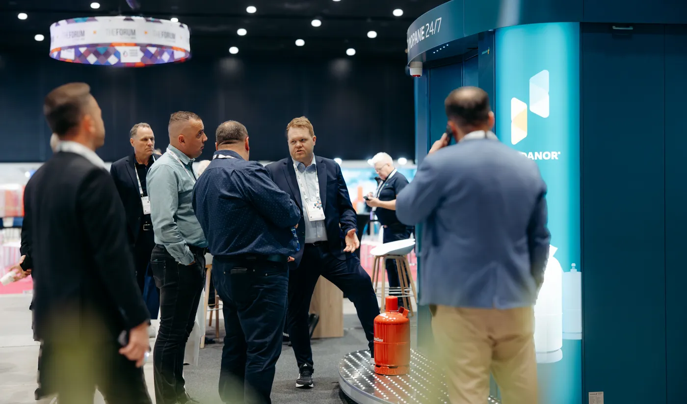 Visitors gather around a teal Vendanor Propane Vending Machine at a trade fair stand, with a propane cylinder on display.