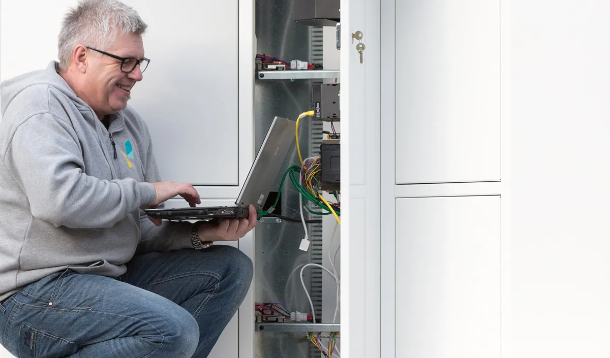 A Vendanor service technician with a laptop performing maintenance inside an open vending machine cabinet.