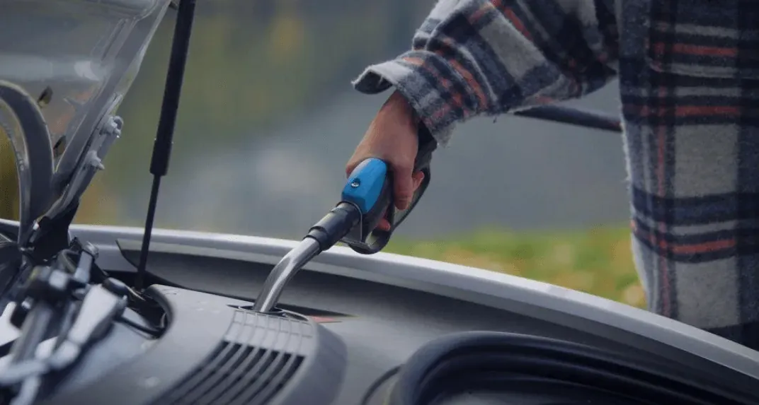 A person using a Vendanor Washer Fluid Dispenser nozzle to fill a car's washer fluid reservoir.