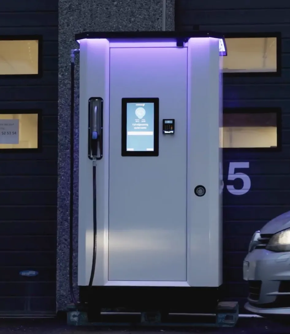A white Vendanor Washer Fluid Dispenser with illuminated touchscreen installed outdoors at dusk beside a parked car.