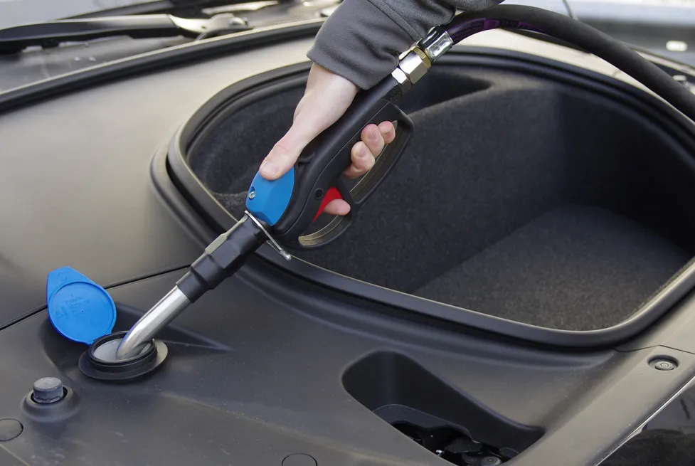 A person uses a Vendanor washer fluid dispenser nozzle to refill a car's windshield washer fluid reservoir under the hood.