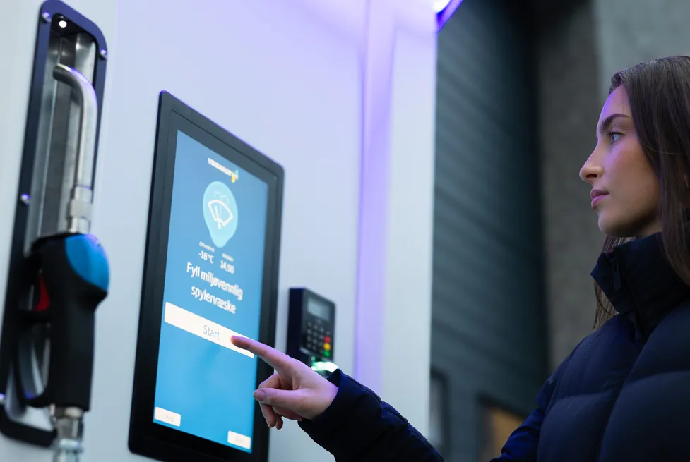 A woman selecting an option on the touchscreen of a Vendanor Washer Fluid Dispenser to fill washer fluid.